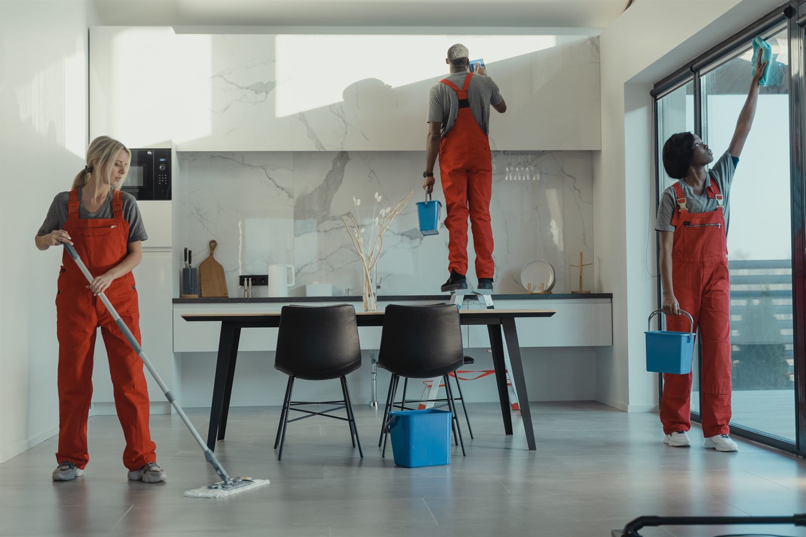 Cleaning team deep cleaning a modern kitchen, wiping cabinets and windows